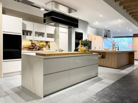 Moderne Küche mit Hochglanzfronten, Kochinsel mit Marmoroptik und eingebauten Elektrogeräten, dazu helle Holzelemente und stylische Hängeleuchten.