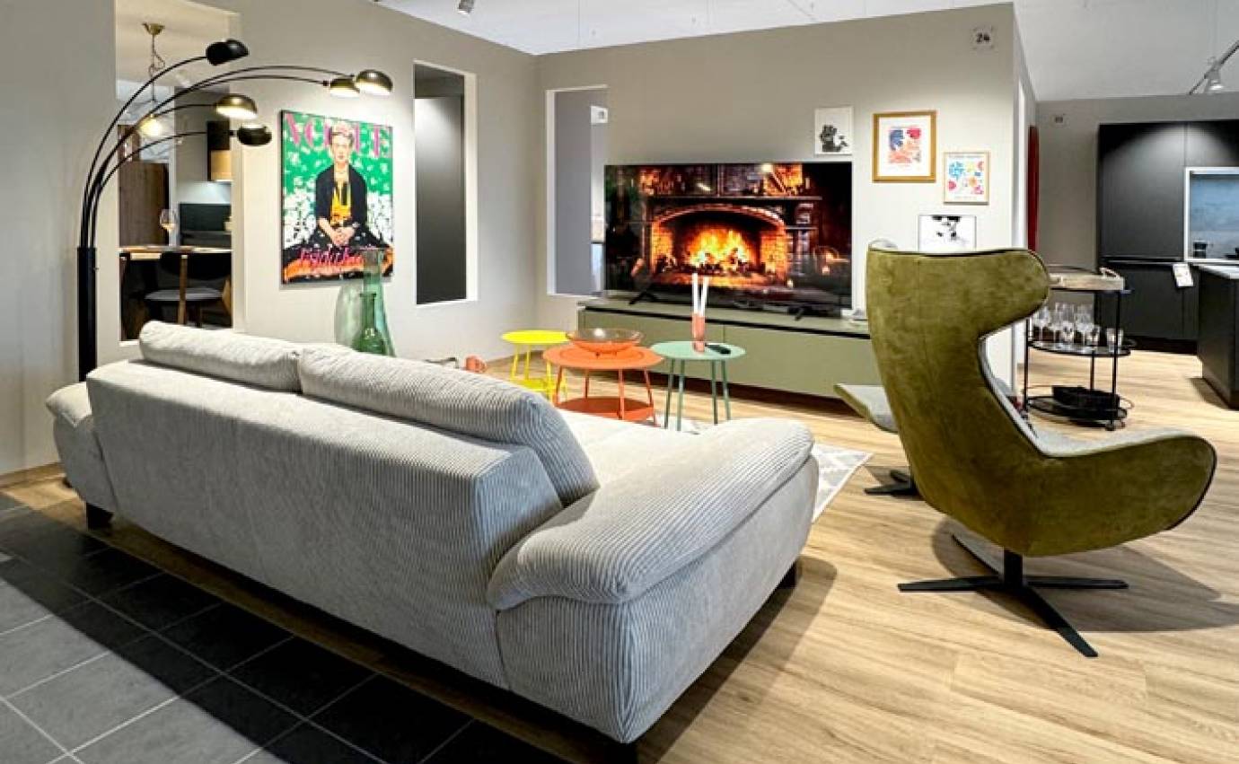 Gemütlicher Wohnbereich mit einem grauen Sofa, lebhaften modernen Kunstwerken und einem lindgrünen Sessel, ergänzt durch einen schlichten Kamin und einen dunklen Kachelboden.