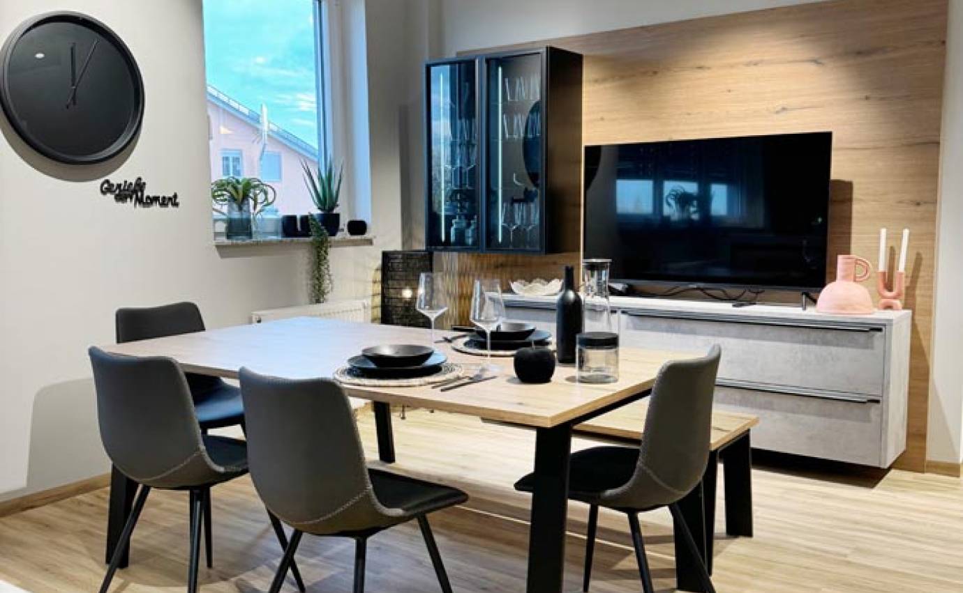 Essbereich grenzt an eine minimalistische Küche mit einem Flachbildfernseher, einem Holztisch, schwarzen Stühlen und einer schicken schwarzen Uhr an der Wand.