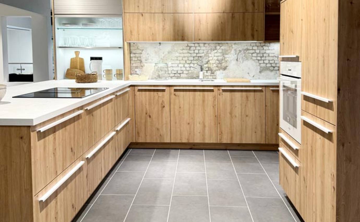 Küchenschränke aus Naturholz mit weißen Arbeitsplatten, rustikalen Steintrennwänden und modernen Geräten, beleuchtet von einer einzigen Hängelampe.