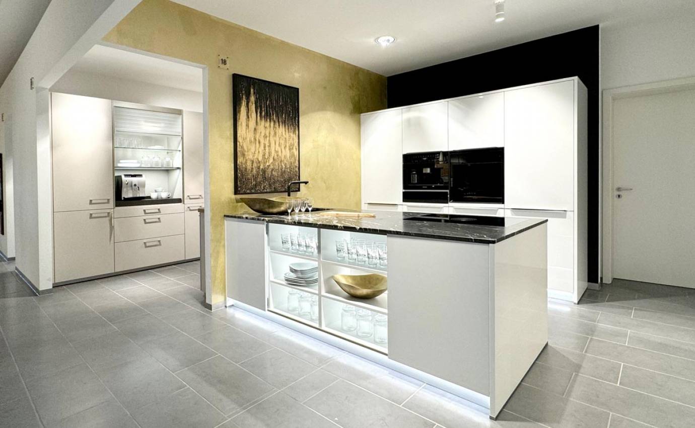 Heller und luftiger Küchenraum mit einer zentralen weißen Insel, hinterleuchteten Glasschränken und einem auffälligen goldenen Gemälde vor einer gelben Akzentwand.