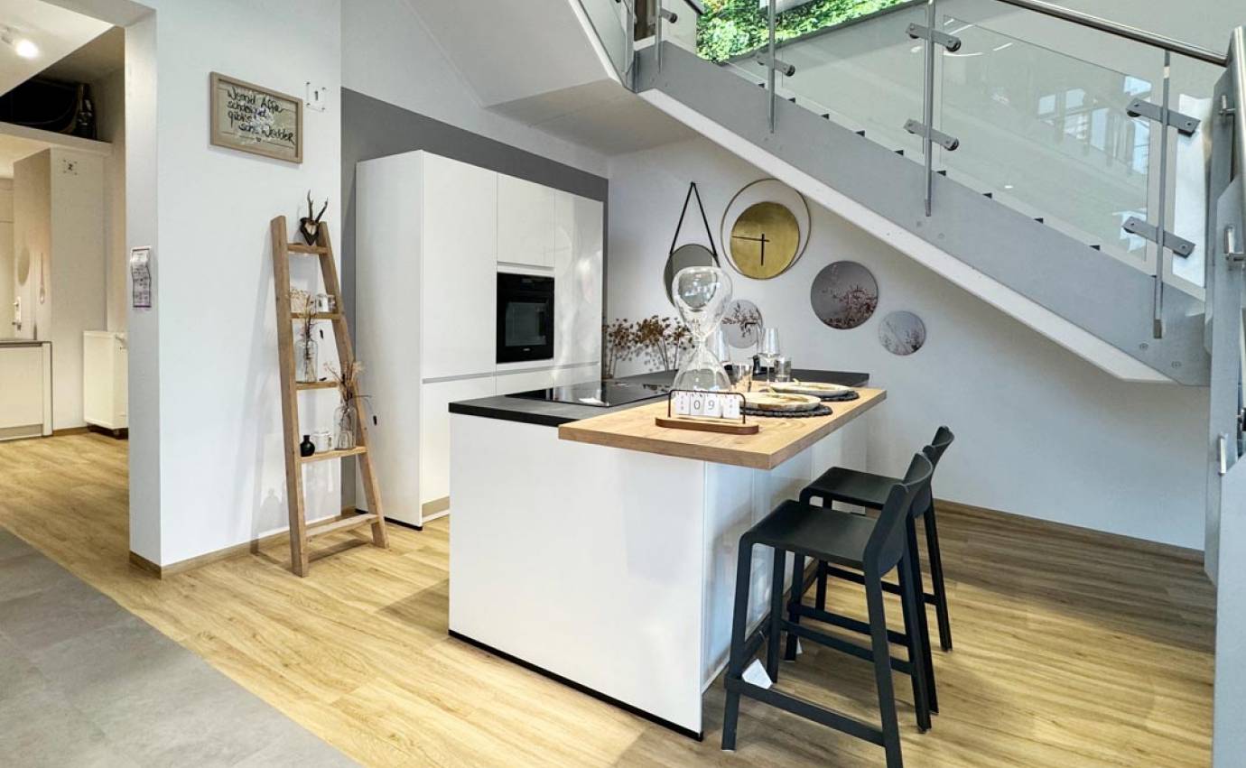 Moderne Küche mit weißer Insel und schwarzen Barhockern, neben einer Glastreppe, mit Holzfußboden und dekorativen Wandplatten.